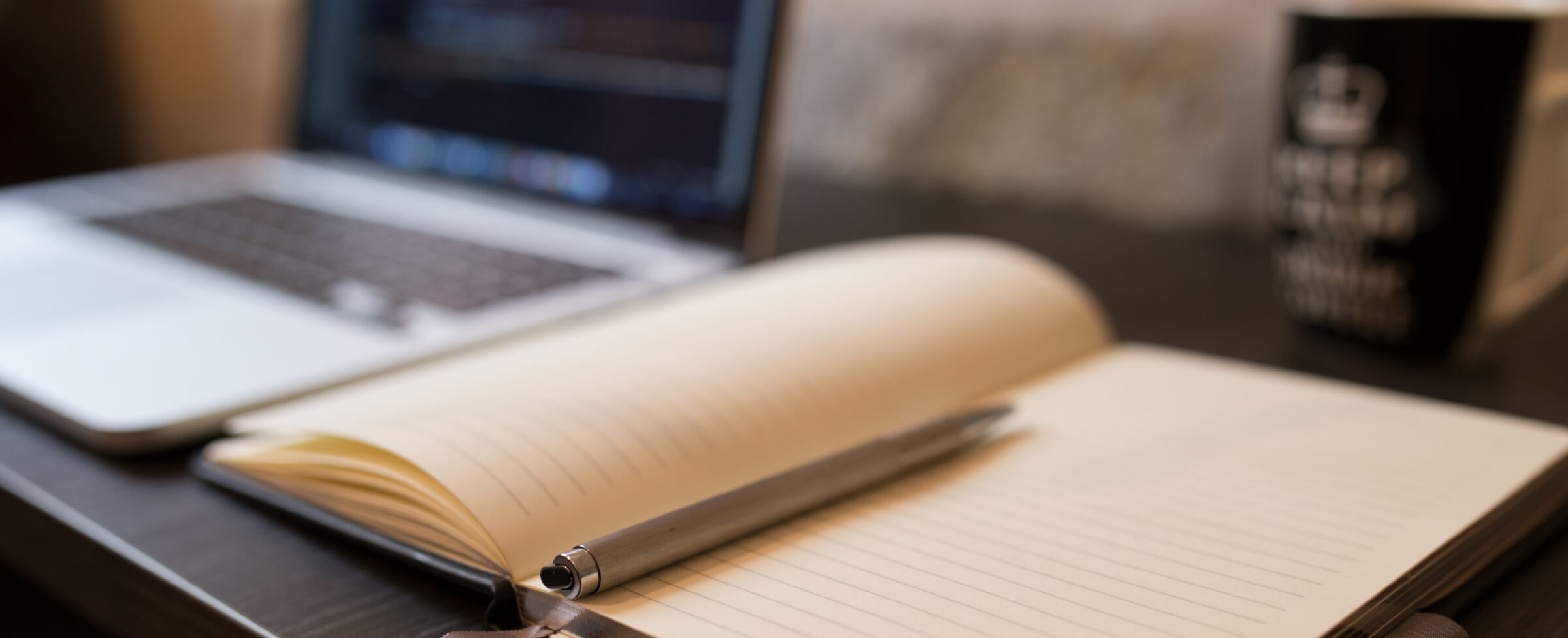 Desktop with a Laptop, open notebook with a pen in the middle and a cup of coffee